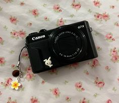 a camera sitting on top of a bed covered in pink flowers and a white bunny keychain