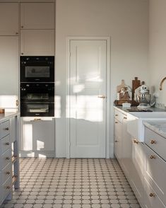 a kitchen with white cabinets and an oven on the wall, next to a tiled floor