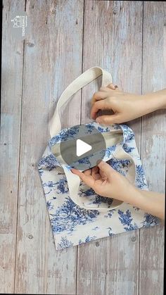 two hands holding onto a blue and white tote bag on top of a wooden floor