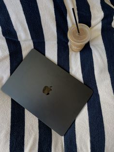 an apple laptop sitting on top of a blue and white striped blanket next to a drink