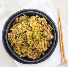 a black bowl filled with noodles and meat on top of a white napkin next to chopsticks