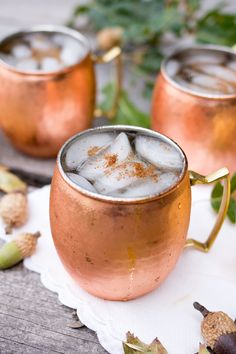 two copper mugs filled with ice sitting on top of a white napkin next to leaves