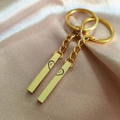 two gold key chains attached to each other on a pink satin surface with an emoticive smiley face in the middle