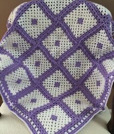 a purple and white crocheted afghan sitting on top of a chair