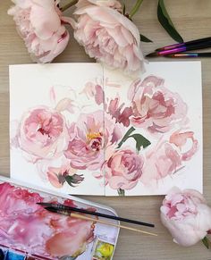 some pink flowers are sitting on a table next to paint and watercolor pencils