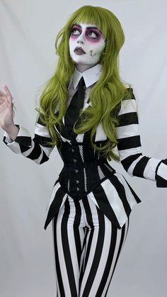 a woman with green hair and makeup is dressed in black and white striped clothing, holding her hands out to the side