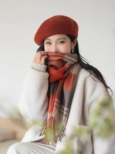 a woman wearing a red hat and scarf with her hands on her face while sitting down