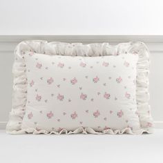 a white pillow with pink flowers and ruffles on the bottom, sitting against a wall