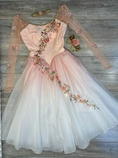 a white dress with pink flowers on the bottom and long sleeves is sitting on a wooden floor