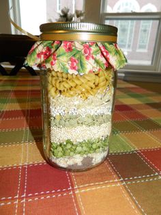 a glass jar filled with pasta and beans on top of a checkered table cloth