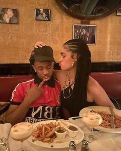 two people sitting at a table with plates of food in front of them and one person covering his mouth