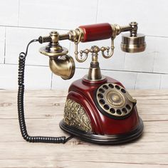 an old fashioned red and gold phone on a wooden table