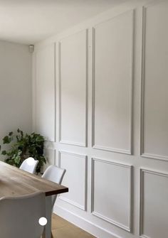 a dining room table with white chairs and a potted plant on the wall behind it