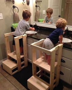 two young boys are playing in the bathroom mirror with their own wooden step stools