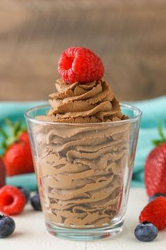 a dessert in a glass with chocolate frosting and raspberries on the side