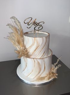 a three tiered cake with gold feathers on top and the word love spelled in cursive letters