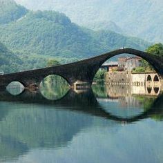 an old stone bridge over a river with mountains in the background