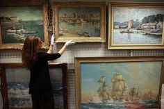 a woman in black shirt and white gloves pointing at paintings on the wall with sailboats