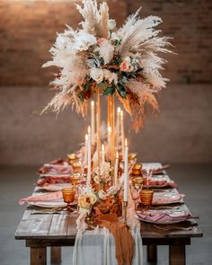 a table topped with lots of candles and flowers next to a tall vase filled with feathers