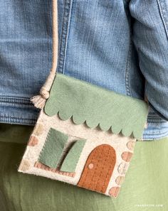 a woman is holding a small purse with a house on the front and side of it