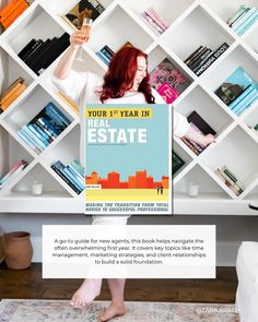 a woman holding up a real estate sign in front of a bookshelf filled with books