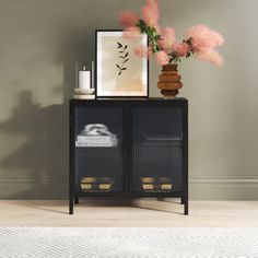 a vase with pink flowers on top of it next to a black cabinet and white rug