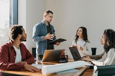 a group of people sitting around a table with laptops and papers in front of them