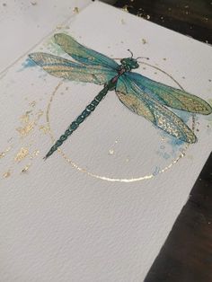 a blue dragonfly sitting on top of a piece of paper with gold flecks