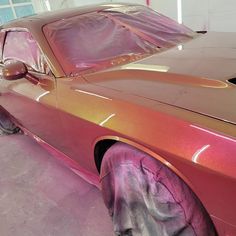 a pink car is parked in a garage with purple paint on it's hood