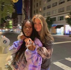 two women standing next to each other in the street with their arms around one another