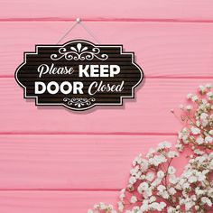 a sign that says please keep door closed on a pink background with flowers in the foreground