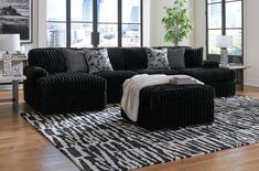 a living room filled with black couches next to large windows and a rug on top of a hard wood floor