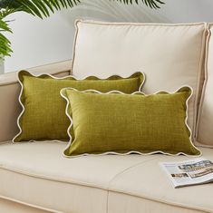 two green pillows sitting on top of a couch next to a potted palm tree