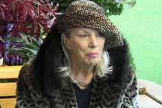 an older woman sitting on a bench wearing a hat and fur coat with her mouth open