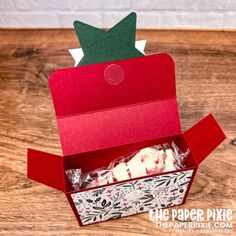 an open red box with white frosting inside on a wooden table next to a piece of paper