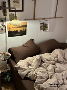 an unmade bed in a room with pictures hanging on the wall and posters above it