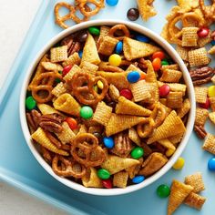 a bowl filled with cereal and pretzels on top of a blue tray next to candy