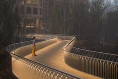 a person standing on a bridge in the middle of a park at night with buildings in the background