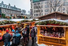 many people are shopping at an outdoor christmas market in the city on a snowy day