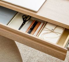 an open drawer with some books and pencils in it on a desk next to a laptop