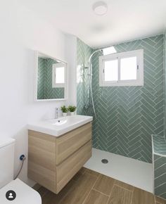 a white toilet sitting next to a bathroom sink under a window in a green tiled wall