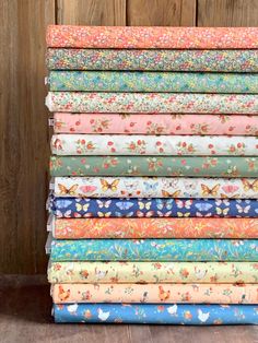 a stack of colorful fabric on top of a wooden floor next to a fence with butterflies and flowers