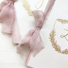 two wedding cards with pink ribbons tied to them and the initials are gold on white paper