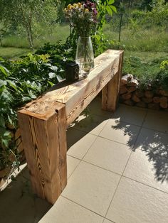 a wooden bench sitting on top of a tiled floor next to plants and flowers in a vase