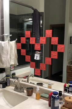 a bathroom sink with red sticky notes attached to the mirror