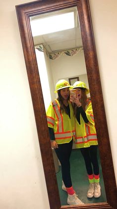 two women in yellow safety vests taking a selfie in front of a mirror