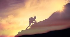 the silhouette of a person climbing up a hill at sunset or sunrise with clouds in the background