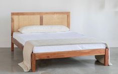 a wooden bed frame with white sheets and pillows on top of it, in an empty room