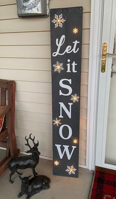 a wooden sign that says let it snow next to a deer statue on the front porch