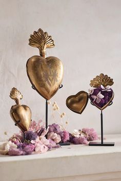 three heart shaped ornaments sitting on top of a white table next to flowers and plants